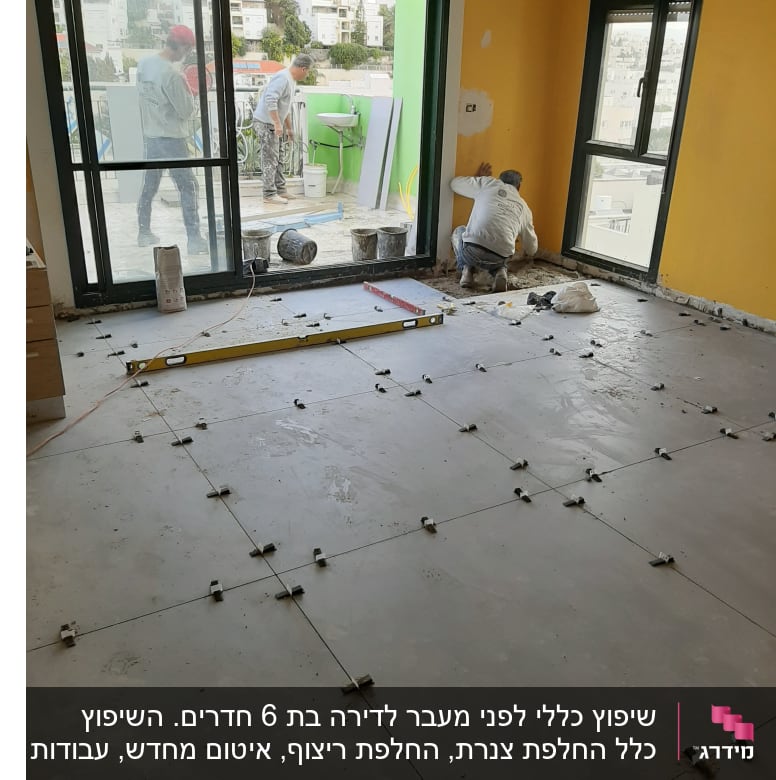 עובדים מתקינים אריחים על רצפה בחדר עם חלונות גדולים